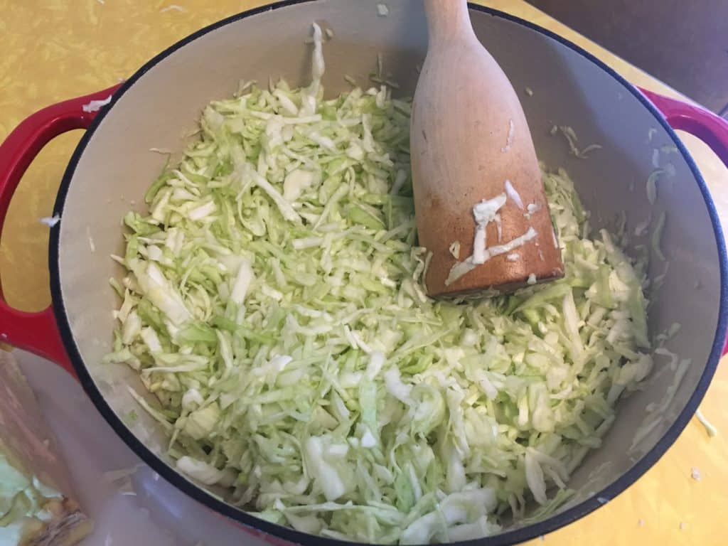 shredded and salted cabbage getting pounded down to break down plant before putting in jar for fermentation 