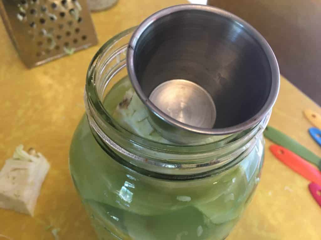 using a cup to hold sauerkraut in jar to keep it in anaerobic environment 